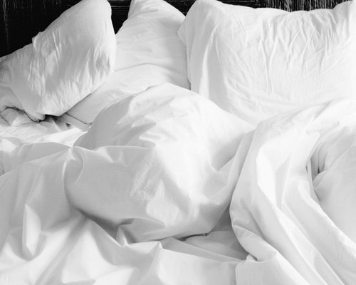 A peaceful brightly lit bedroom with white linen sheets on a comfortable bed