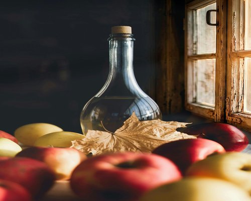 A glass bottle with crystal clear water standing next to fresh red apples